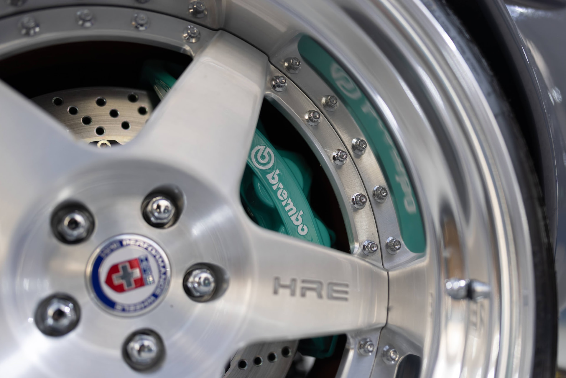 Macro detail of a polished HRE forged wheel and teal Brembo brake caliper on a show car at the SEMA Show