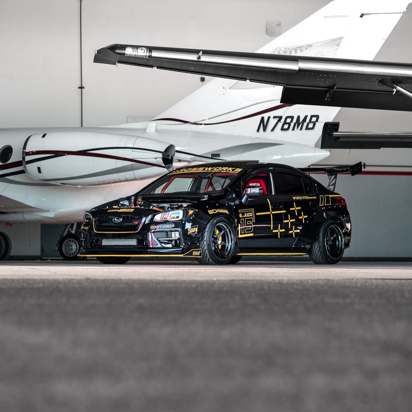Black and yellow Subaru WRX race car parked beside a private jet inside a hangar