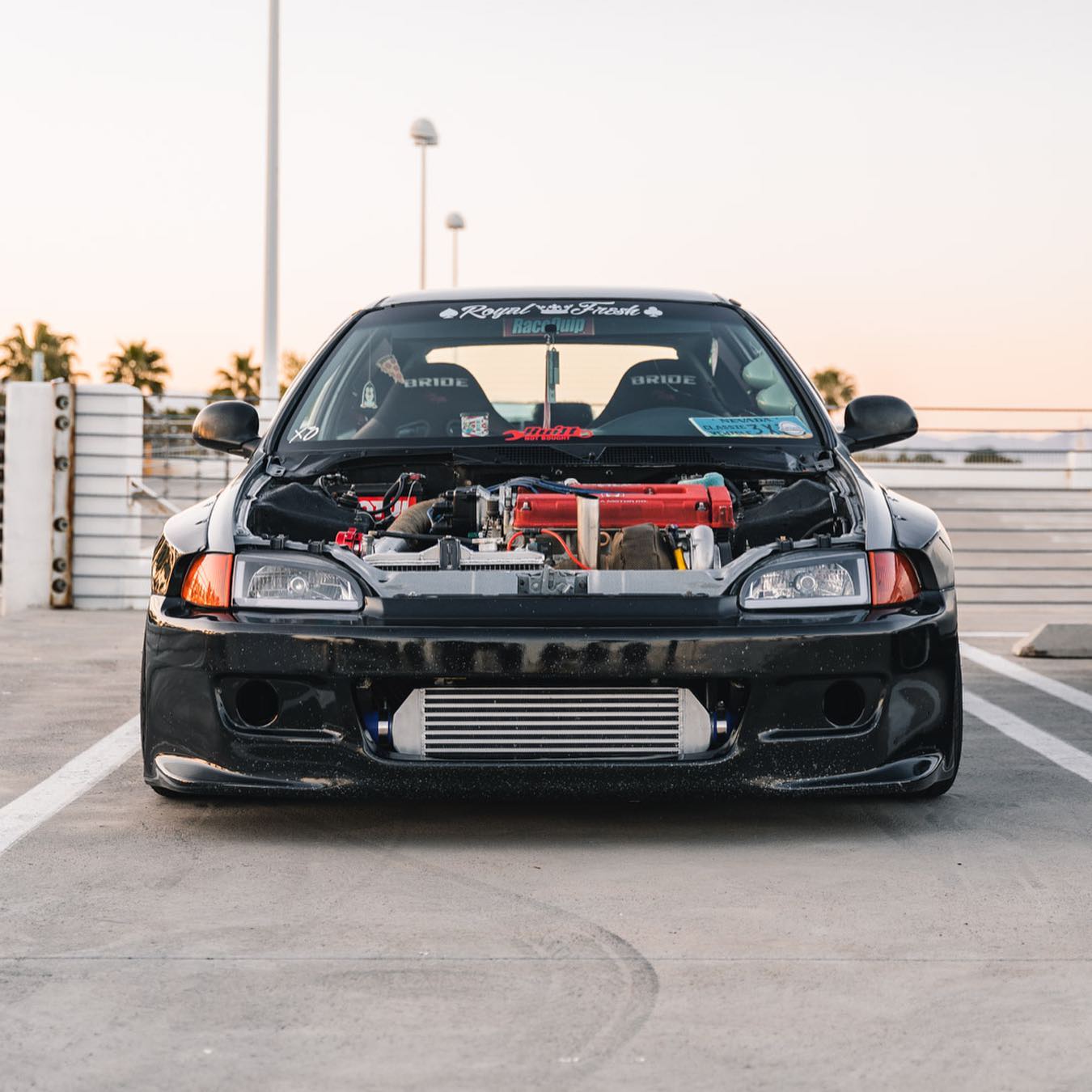 Black Honda Civic EG with a turbo build, front mount intercooler, and Bride seats shot head on in a Las Vegas parking structure at sunset