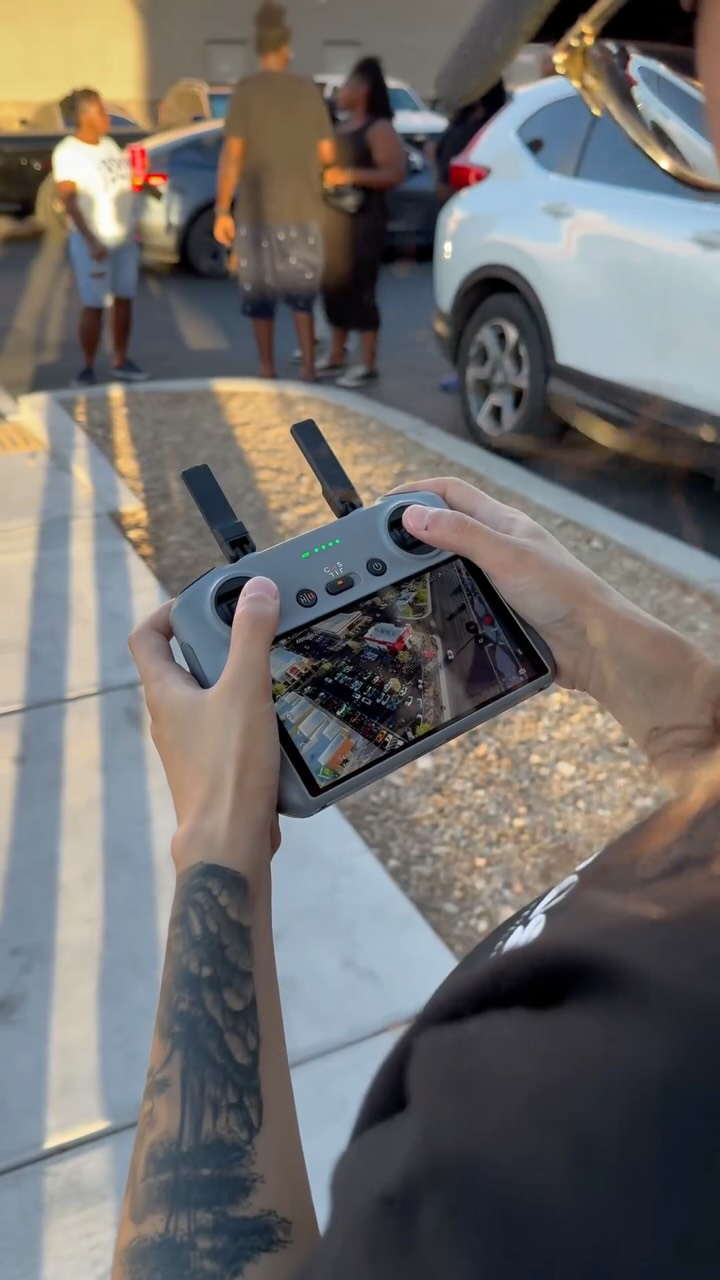 Crew member flying a drone with an aerial view of a car event on the controller screen