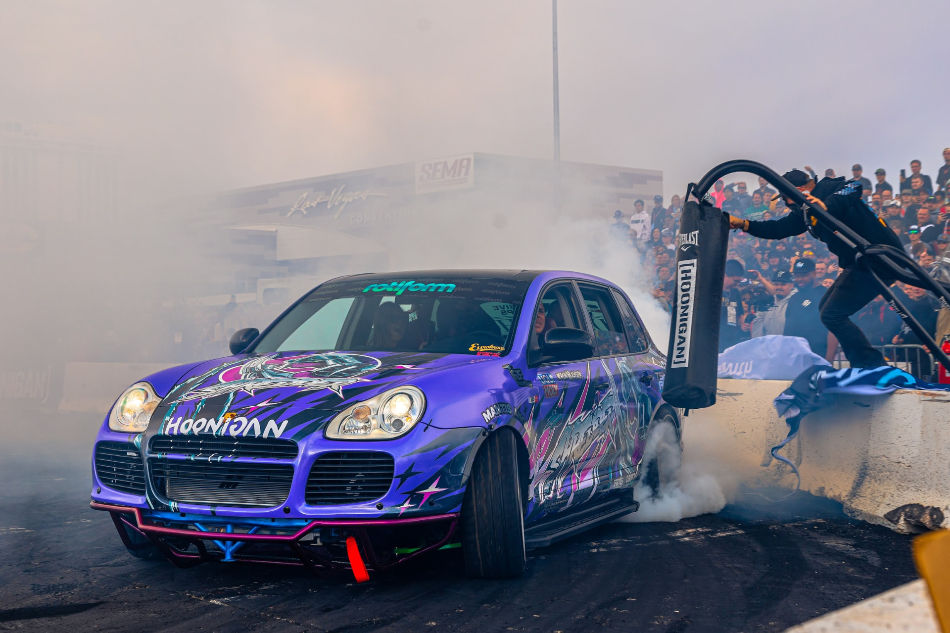 Purple wrapped Hoonigan Porsche Cayenne doing a smoking burnout in front of the Las Vegas Convention Center at SEMA Ignited