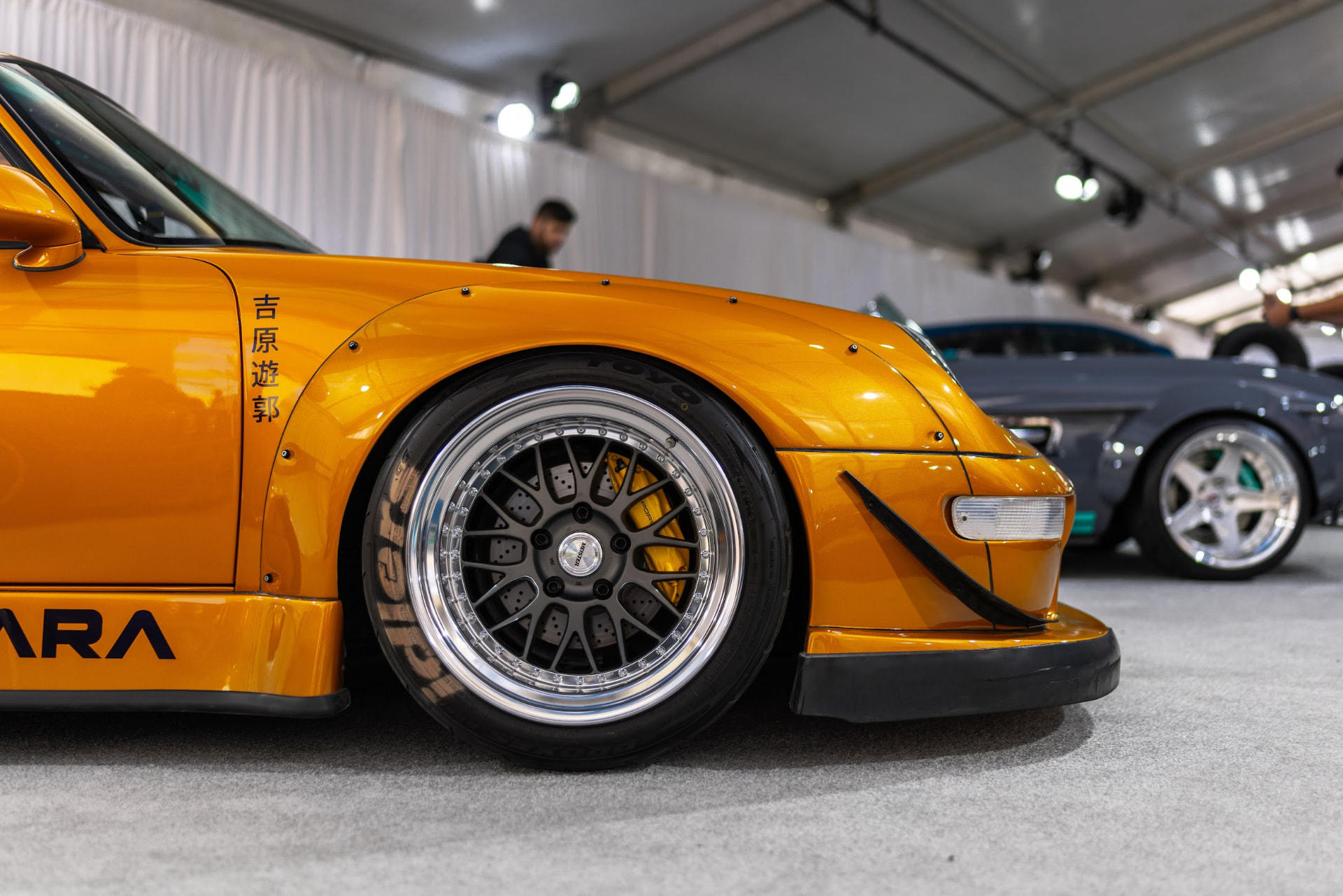 Orange RWB widebody Porsche 911 front fender and deep dish wheel detail inside a SEMA Show display tent