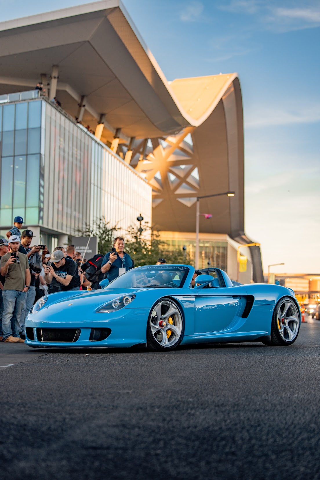 Light blue Porsche Carrera GT rolling out past photographers in front of the Las Vegas Convention Center at sunset during the SEMA Show