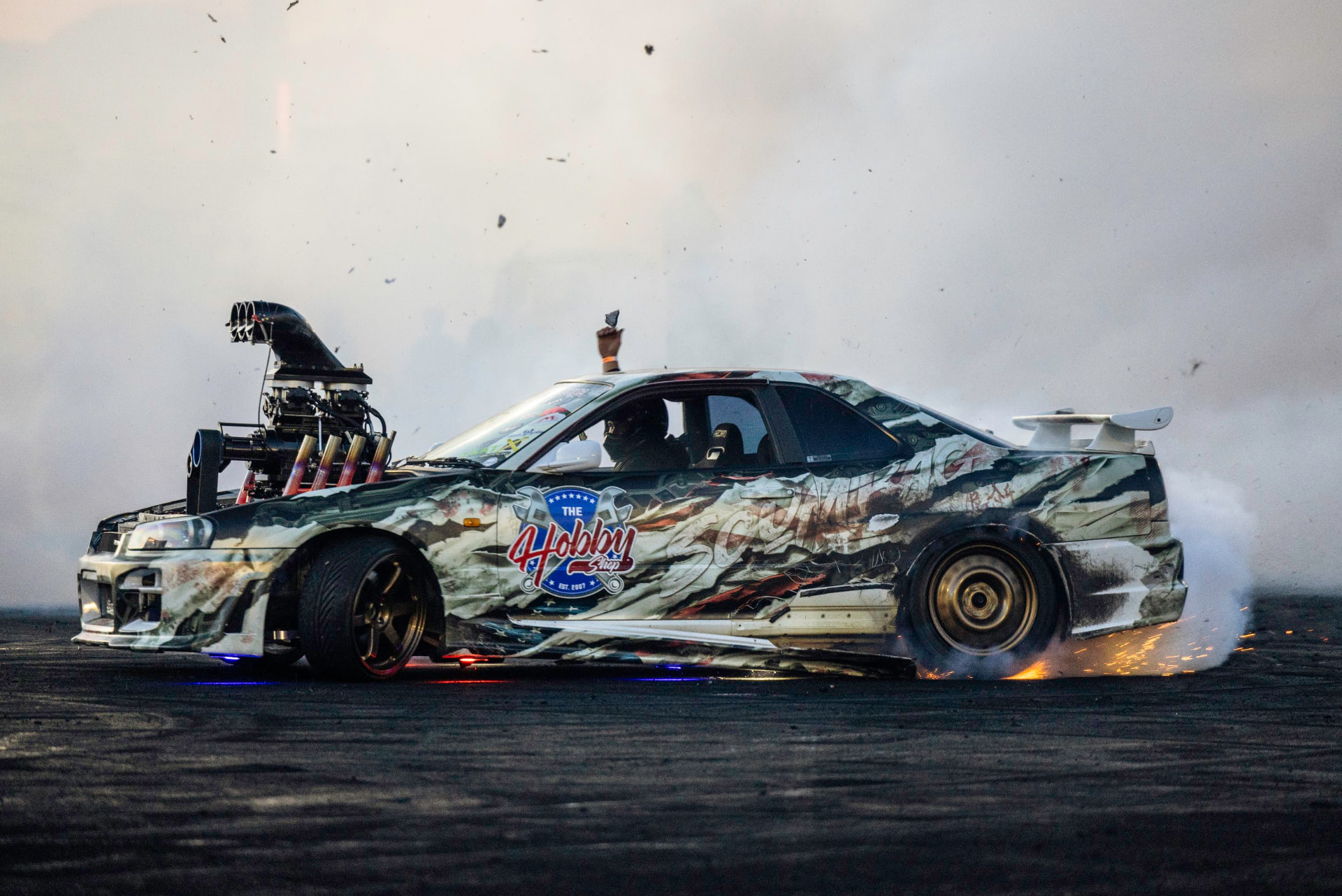 Blown Nissan Skyline R34 with a blower and exposed headers throwing sparks during a burnout at SEMA Ignited