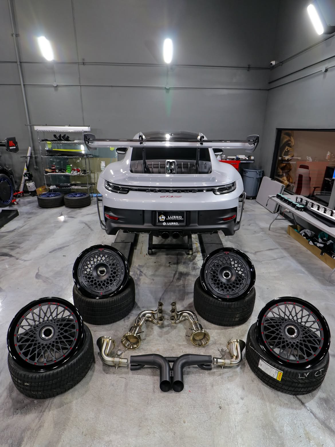 White Porsche 992 GT3 RS on a lift with AL13 wheels and a GMG Racing exhaust system laid out on the shop floor